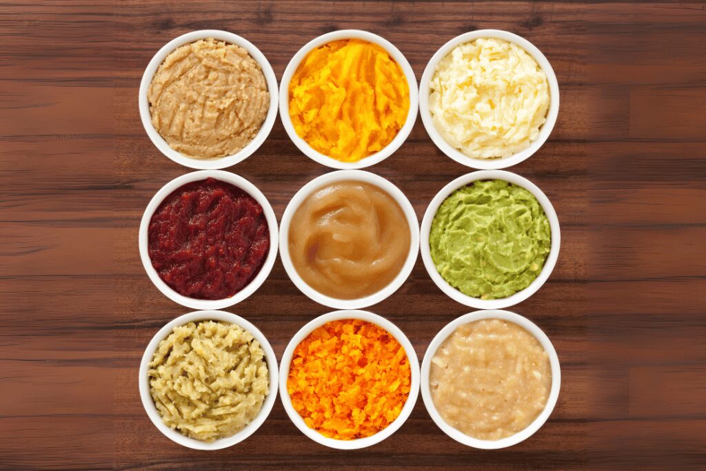 A variety of soft foods such as yogurt, mashed potatoes, scrambled eggs, and applesauce in small white bowls